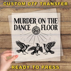 May include: A DTF transfer with the text "MURDER ON THE DANCE FLOOR" above a disco ball and three crows. The words "CUSTOM DTF TRANSFER" and "READY TO PRESS" are also printed on the transfer.