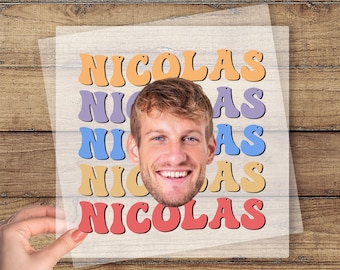 May include: A custom DTF transfer featuring the name "NICOLAS" in retro-style lettering, with a smiling face in the center. The design includes orange, purple, blue, and red text. The words "CUSTOM DTF TRANSFER" and "READY TO PRESS" are also visible.
