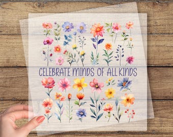 May include: A clear DTF transfer sheet featuring a watercolor floral design with various colorful flowers and the text "CELEBRATE MINDS OF ALL KINDS". The words "CUSTOM DTF TRANSFER" and "READY TO PRESS" are also visible.
