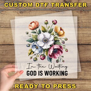 May include: A floral DTF transfer featuring a bouquet of colorful flowers, including white, pink, and orange blooms, with green leaves. The text "In the Waiting GOD IS WORKING" is displayed below the flowers. The words "CUSTOM DTF TRANSFER" and "READY TO PRESS" are also visible.