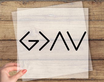 May include: A clear transfer sheet with the black letters "G > AV" is held by a hand. The words "CUSTOM DTF TRANSFER" and "READY TO PRESS" are printed in yellow above and below the design. The background is a wooden surface.