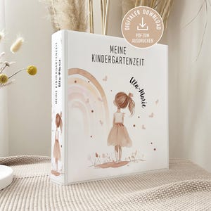 Puede incluir: Una carpeta blanca con el texto "MEINE KINDERGARTENZEIT" y "Ulla-Marie". La portada presenta una ilustración en acuarela de una niña con un vestido, un arcoíris y mariposas. Un icono de descarga digital está en la esquina superior derecha.