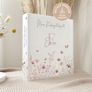 Könnte beinhalten: Ein weißer Ordner mit floralen und Schmetterlingsillustrationen. Der Ordner trägt den Text "Meine Kindergartenzeit" und den Namen "Emma". Ein Symbol für digitalen Download ist sichtbar.