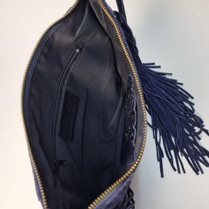 Puede incluir: Bolso de mano de ante azul marino con cremallera dorada y largos flecos. El interior es negro con un peque&ntilde;o bolsillo con cremallera. El bolso tiene un asa peque&ntilde;a y est&aacute; abierto.