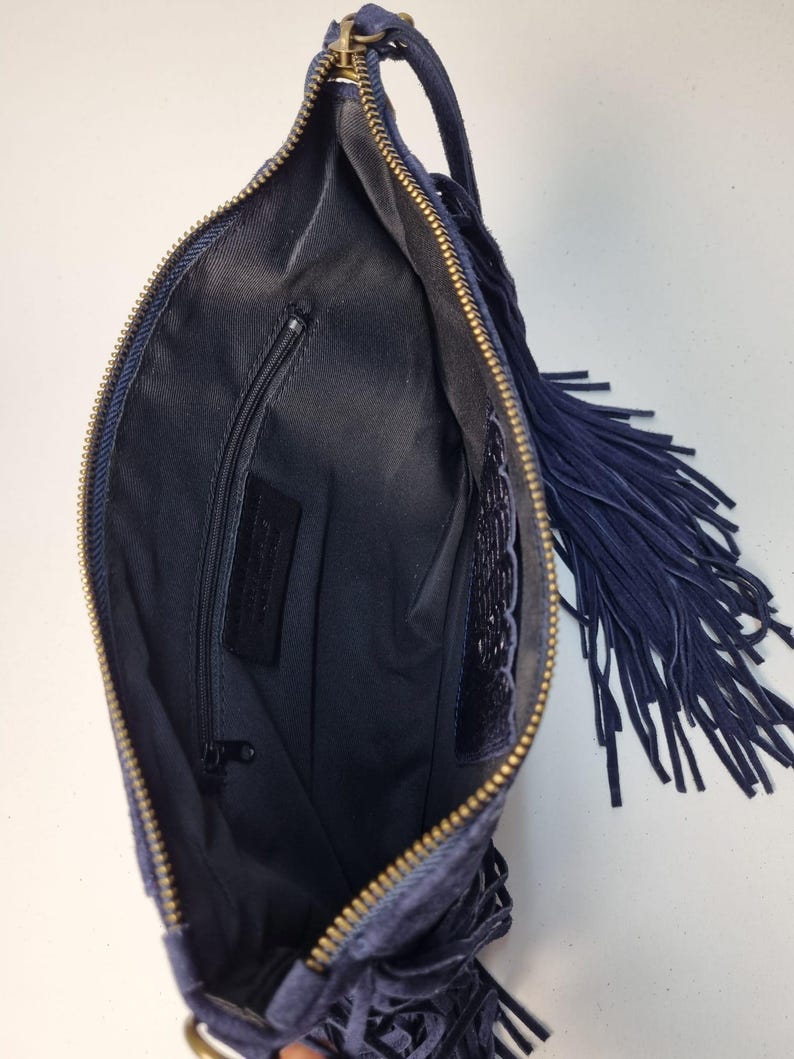Puede incluir: Bolso de mano de ante azul marino con cremallera dorada y largos flecos. El interior es negro con un peque&ntilde;o bolsillo con cremallera. El bolso tiene un asa peque&ntilde;a y est&aacute; abierto.