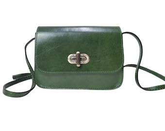 May include: A small green leather crossbody bag with a brass clasp closure. The bag has a short strap and a long adjustable strap.