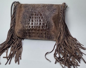 May include: Brown leather crossbody bag with a crocodile-skin texture on the front. The bag features long, flowing fringe on the sides and a shoulder strap. The bag is a medium brown color.