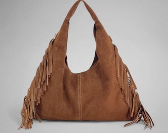 May include: A brown suede hobo bag with long fringe detailing. The bag has a curved shape with a single shoulder strap and a stitched seam down the center. The fringe is along the sides of the bag.
