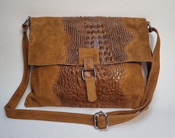 May include: A brown leather crossbody bag with a flap closure. The bag features a textured crocodile-like pattern on the front and flap, with a suede-like texture on the sides. It has a long adjustable strap and a silver buckle.