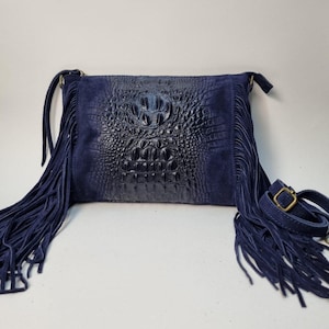 Puede incluir: Bolso bandolera azul marino con un panel central con relieve de cocodrilo y flecos de ante. El bolso tiene una correa ajustable y una hebilla met&aacute;lica. El bolso mide aproximadamente 25 cm de ancho y 20 cm de alto.