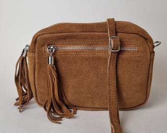May include: A brown suede crossbody bag with a rectangular shape. The bag features a zipper closure, a long adjustable strap, and decorative tassels on the side. The hardware is silver-toned.