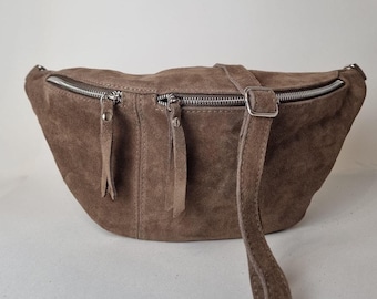 May include: A brown suede fanny pack with two zippered compartments and a silver-tone zipper. The adjustable strap and the zipper pulls are made of the same suede material. The bag has a curved shape.