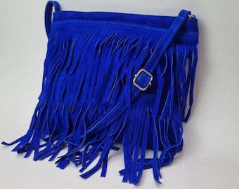 May include: A vibrant blue suede crossbody bag with long fringe detailing. The bag features a matching adjustable strap and a silver-toned buckle closure. The bag's design is a bohemian style, perfect for carrying essentials.
