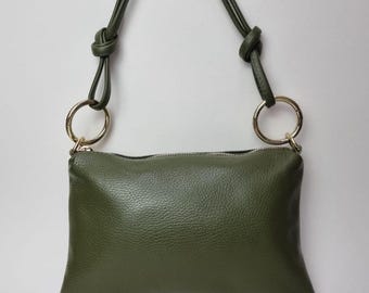May include: Olive green rectangular crossbody bag with a textured surface. The bag features a gold zipper and two gold-colored rings connecting the strap to the bag. The strap is olive green and knotted at the top.