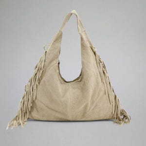 May include: A beige suede hobo bag with a single shoulder strap and long fringe detailing along the sides. The bag has a curved opening and a soft, slouchy design, perfect for everyday use.