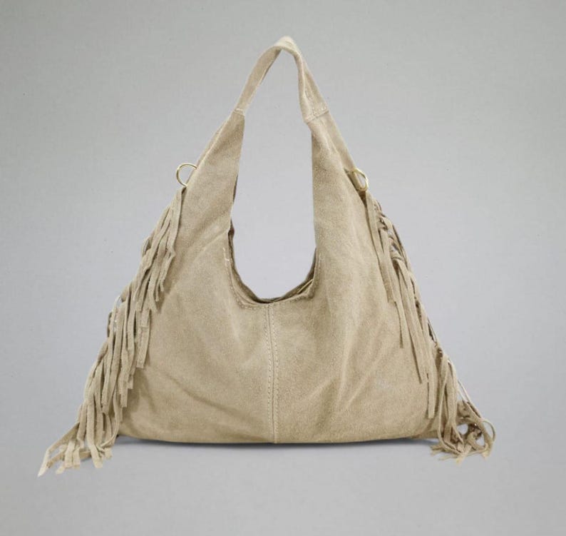 May include: A beige suede hobo bag with a single shoulder strap and long fringe detailing along the sides. The bag has a curved opening and a soft, slouchy design, perfect for everyday use.