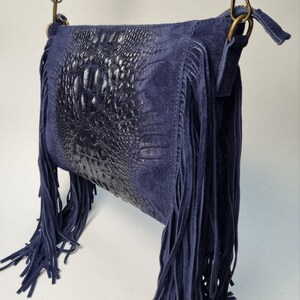 Puede incluir: Un bolso bandolera de ante azul marino con un panel central de cuero con relieve de cocodrilo. El bolso presenta largos flecos y una correa ajustable a juego. Los herrajes son de color lat&oacute;n.
