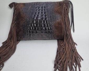 May include: A brown leather clutch with a crocodile-textured center panel and suede side panels. The clutch features long, dangling fringe on both sides, adding a bohemian flair to the design.