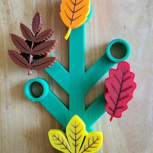 May include: A green, tree-shaped decorative item with five colorful, stylized leaves. The leaves are in shades of yellow, orange, red, and brown. The item is placed on a wooden surface.
