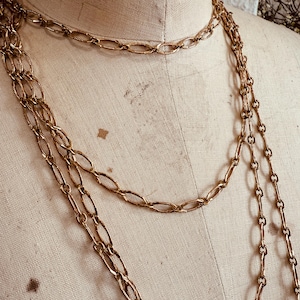 May include: Gold-toned necklaces with various chain link designs. The necklaces are draped on a mannequin, showcasing the different lengths and styles. The chains have a vintage aesthetic.