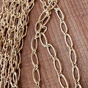 May include: Close-up of gold-colored chain necklaces with various link designs. The chains are arranged on a wooden surface, showcasing the different textures and patterns of the jewelry. The chains are likely for fashion or jewelry making.