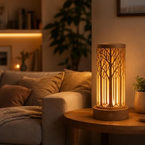 May include: A wooden table lamp with a tree design. The lamp has a cylindrical shape with a carved forest silhouette, emitting a warm, inviting glow. The lamp sits on a round wooden table next to a small potted plant.