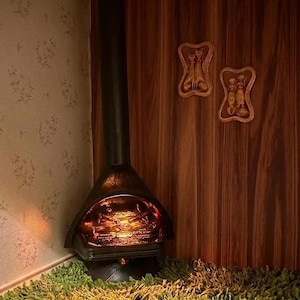 May include: A vintage black fireplace with a glowing fire inside, set against a wood-paneled wall. The fireplace sits on a green shag rug, with two framed cat figurines on the wall.