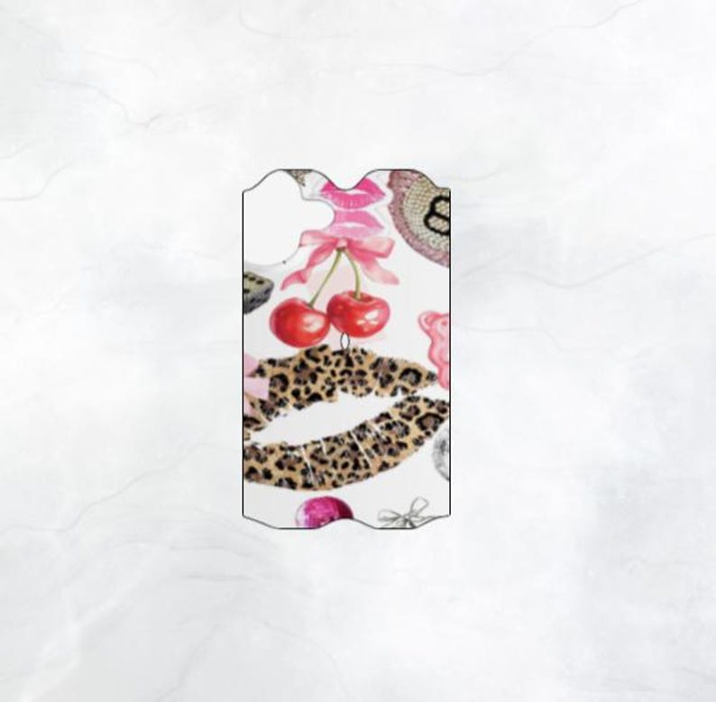 May include: A white background with a pink and red cherry design. The cherries are on a stem with green leaves. The cherries are surrounded by a leopard print lip design. There are other pink and red designs around the cherries and lip.