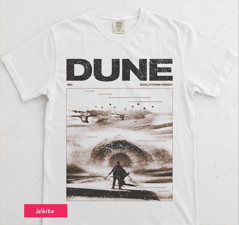 May include: White t-shirt featuring the word "DUNE" in large black letters, with the text "NOVEL BY FRANK HERBERT" below. The shirt displays a sepia-toned graphic from the novel, including a figure in a desert landscape. The year "1965" is also printed.