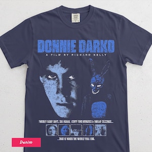 May include: Navy blue t-shirt featuring the movie title "DONNIE DARKO" in distressed blue lettering. The shirt includes a graphic of a person's face and a rabbit. Text on the shirt reads "TWENTY EIGHT DAYS, SIX HOURS, FORTY TWO MINUTES & TWELVE SECONDS..."