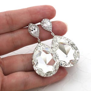 May include: A pair of silver teardrop earrings with large clear crystal stones. The stones are surrounded by smaller clear crystals.