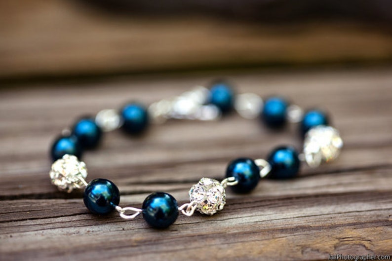 May include: A bracelet featuring dark teal beads and sparkling silver accents. The bracelet is strung on a silver chain and has a clasp closure. The beads are interspersed with clusters of small, glittering crystals.