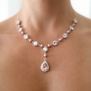 May include: A delicate necklace featuring a series of round, clear crystals set in a gold-toned metal. The necklace has a teardrop-shaped pendant with a large, light pink stone. The necklace is designed to be worn around the neck.