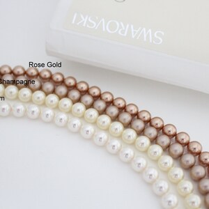 May include: Strands of Swarovski crystal pearls in White/Ivory, Cream, Champagne, and Rose Gold. The image shows the pearls' color variations, with the Swarovski logo visible in the background. The pearls are approximately 8 mm in size.
