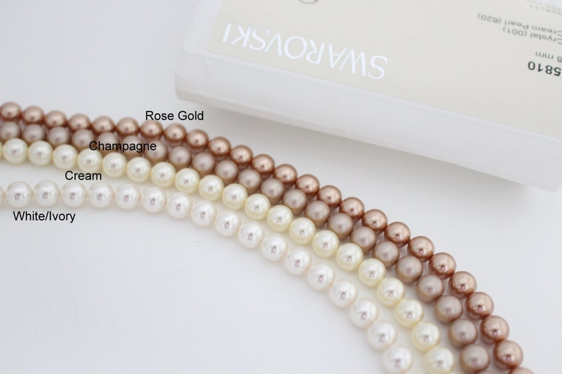 May include: Strands of Swarovski crystal pearls in White/Ivory, Cream, Champagne, and Rose Gold. The image shows the pearls' color variations, with the Swarovski logo visible in the background. The pearls are approximately 8 mm in size.