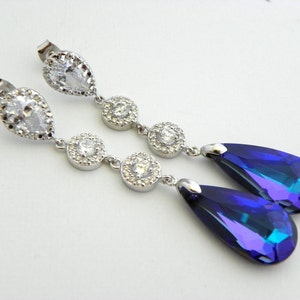 May include: A pair of elegant drop earrings. Each earring features a clear, pear-shaped stone at the top, followed by three round, clear stones. The earrings end with a large, teardrop-shaped, iridescent blue stone.