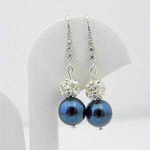 May include: A pair of dangle earrings featuring dark blue, iridescent pearl-like beads. Each earring has a silver-toned, crystal-studded top and a large, round bead. The earrings are displayed against a white background.
