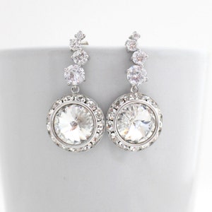 May include: Silver dangle earrings with a large clear crystal surrounded by smaller crystals.
