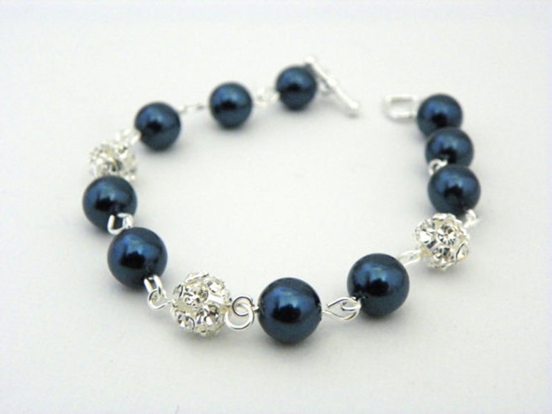 May include: A bracelet featuring dark blue, round beads interspersed with sparkling, silver-toned crystal accents. The bracelet is strung on a silver chain and has a simple clasp.