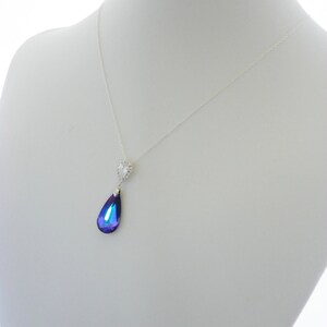 May include: A silver necklace with a teardrop-shaped pendant. The pendant is a deep blue and purple color, with a small, clear, heart-shaped accent at the top. The necklace is displayed on a white mannequin.