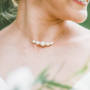 May include: A gold necklace with a series of pearls and small crystals. The necklace is worn on a person's neck, and a matching pear-shaped earring is visible. The image is a close-up, focusing on the jewelry.