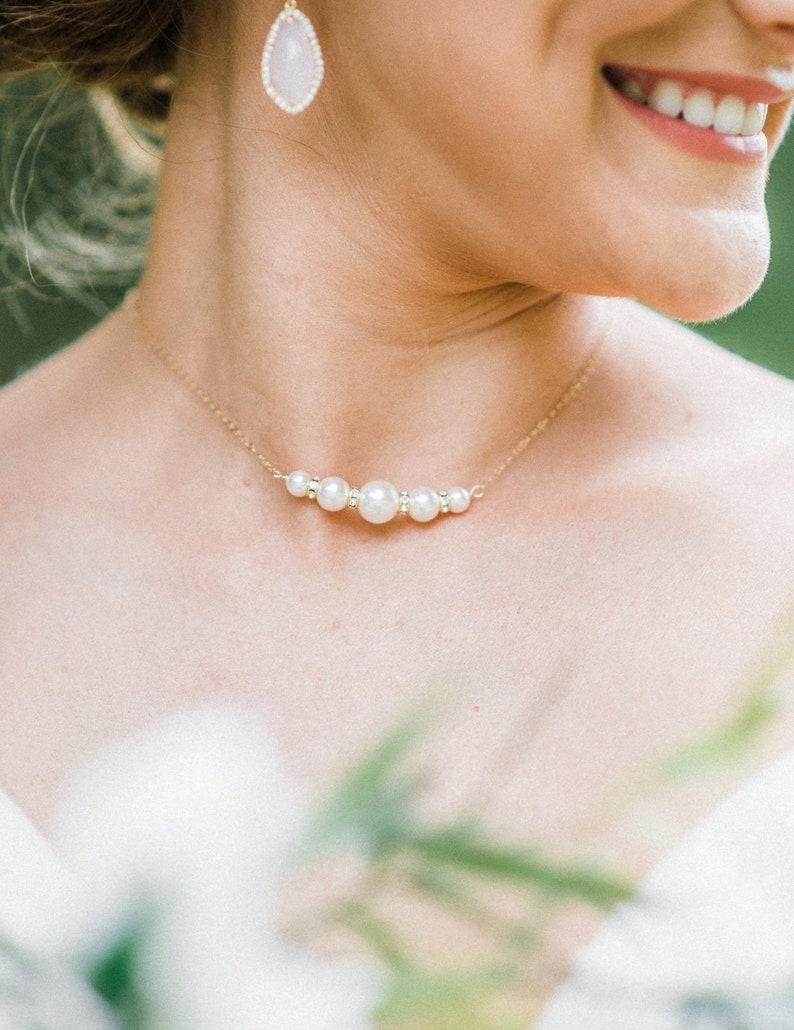 May include: A gold necklace with a series of pearls and small crystals. The necklace is worn on a person's neck, and a matching pear-shaped earring is visible. The image is a close-up, focusing on the jewelry.