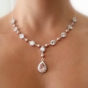 May include: A delicate necklace featuring a series of round and square clear crystals, interspersed with smaller, round beads. The pendant is a pear-shaped crystal. The necklace is a light gold color.