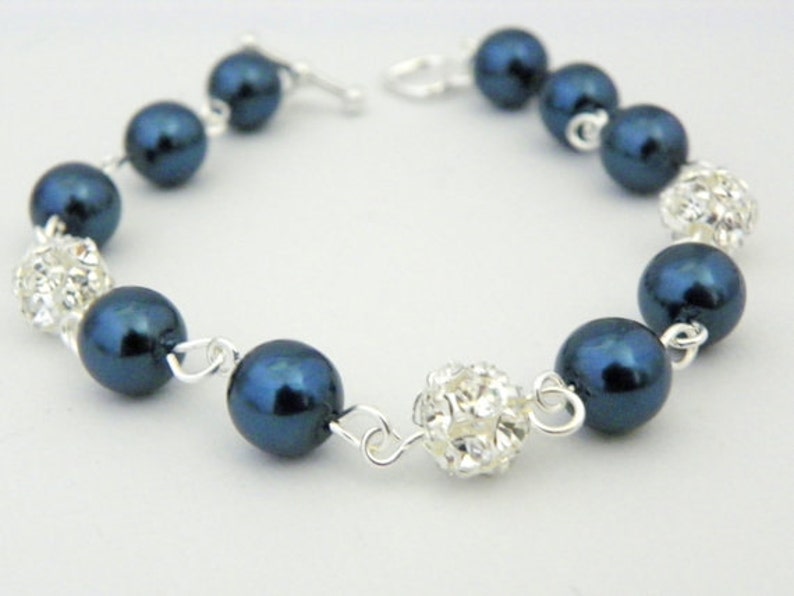 May include: A bracelet featuring navy blue faux pearls and sparkling crystal-covered beads. The beads are strung together with silver-colored chain links and a clasp. This jewelry item is suitable for special occasions.