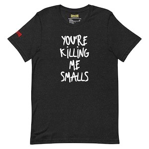 May include: Dark gray t-shirt with the phrase "YOU'RE KILLING ME SMALLS" in white, handwritten-style lettering. The brand name "SHYSTER" is printed at the top and on the left sleeve in red. A casual, unisex tee.