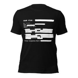 Può includere: T-shirt nera con testo bianco che ricorda un documento governativo oscurato. Il testo include "CASE FILE", "To: Citizens" e "Internal Transparency Report". Il design presenta linee orizzontali che oscurano parte del testo.