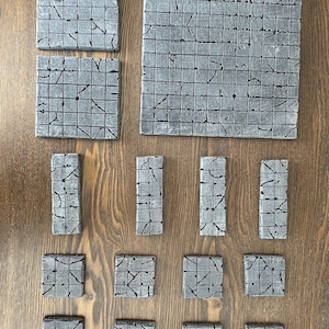 May include: A set of 15 gray and black textured square and rectangular tiles for tabletop gaming. The tiles are made of a durable material and have a realistic stone look.