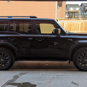 May include: A black SUV with a roof rack and tinted windows. The vehicle is parked on a concrete driveway.