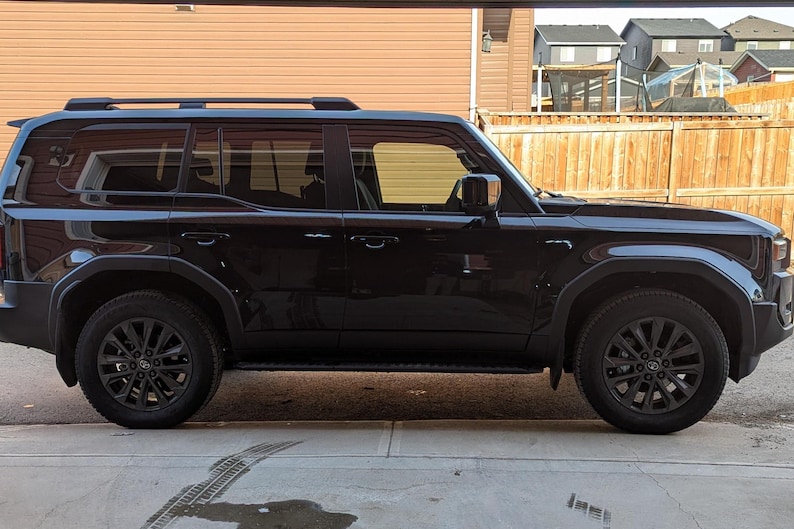 May include: A black SUV with a roof rack and tinted windows. The vehicle is parked on a concrete driveway.
