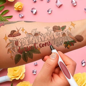 May include: A temporary tattoo on an arm featuring the text "My Anxiety Vacant, con" with mushroom and snail illustrations. A hand holds a white and burgundy marker, with yellow roses and crystals on a pink background.